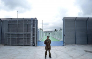 (FILES) An Italian police officer stands in a recently build Italian-run migrant centre at the port of Shengjin, some 60 kms northwest of Tirana, on October 11, 2024. Controversial camps set up in Albania to house migrants rescued in Italian waters are ready to start functioning, the Italian ambassador in Tirana said today. The deal, signed in November by Italian Prime Minister and Albanian counterpart, was sharply criticised by rights groups. They say it is illegal under international law, warning that Albania, a non-EU country offers limited protection for asylum seekers. (Photo by Adnan Beci / AFP)